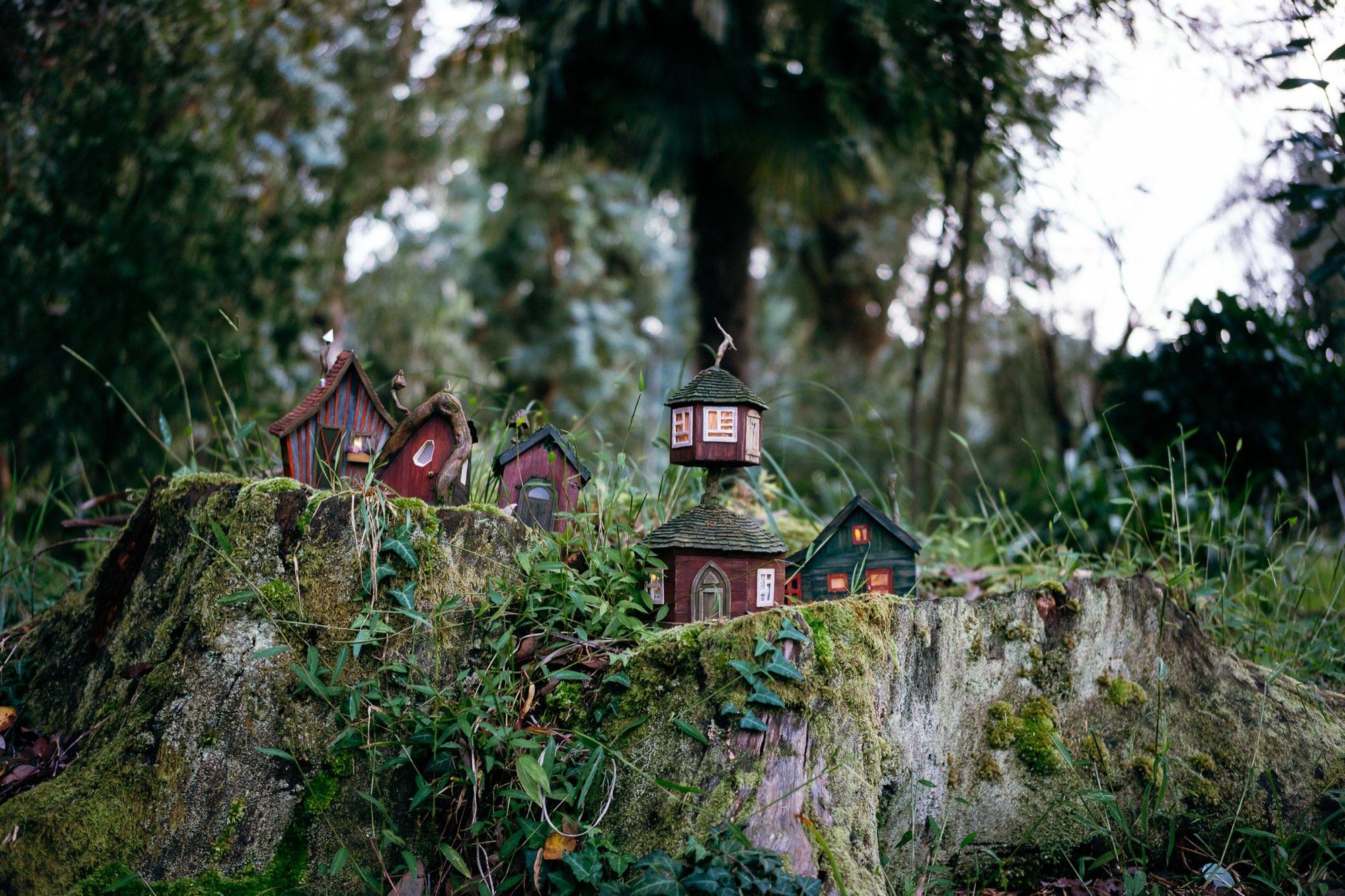 A whole village of miniature lit houses spread along the top of a mossy tree stump in a green forest at dusk