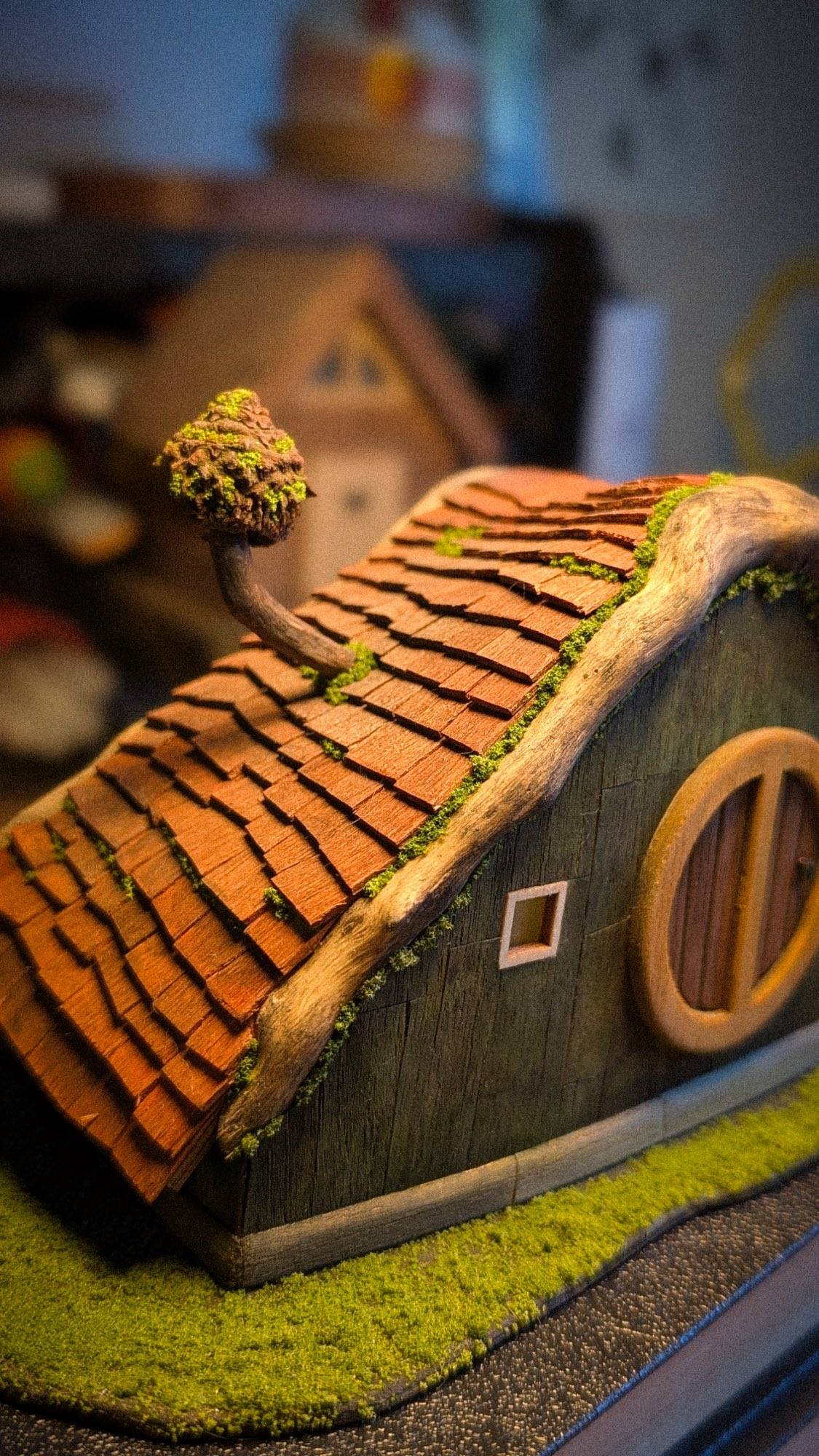 The cottage head on, the round door centred under a moss-topped clay roof