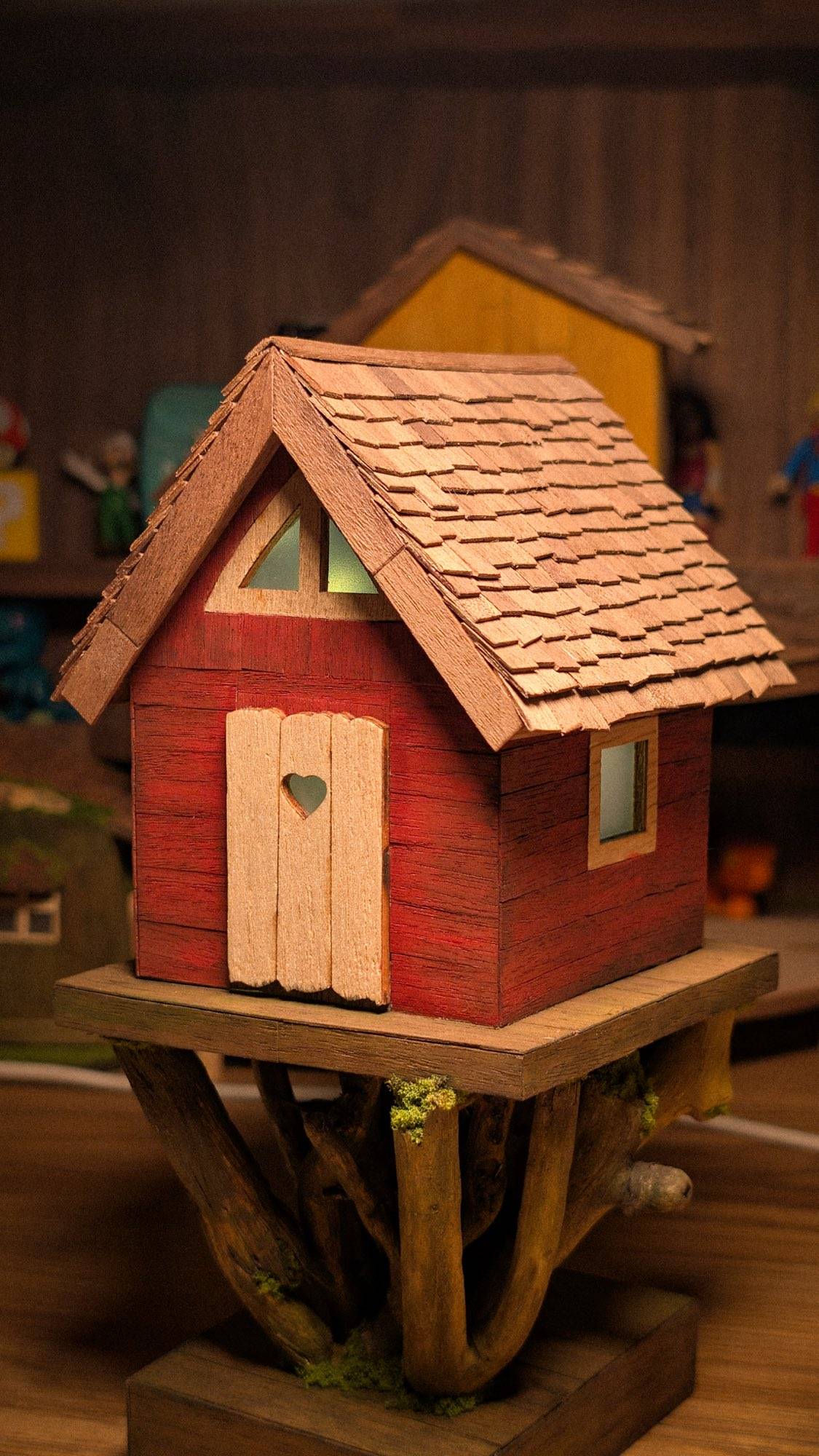 A red cottage with a heart cut into its plank door, standing on a platform of driftwood roots